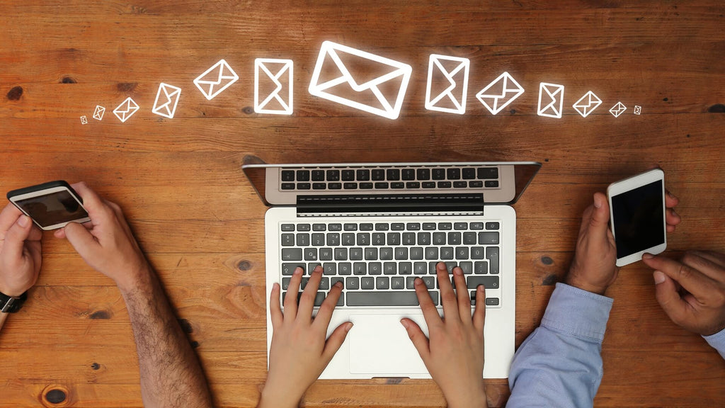 Hands typing on a laptop with email icons flowing towards smartphones, representing email marketing strategies to engage and convert subscribers.