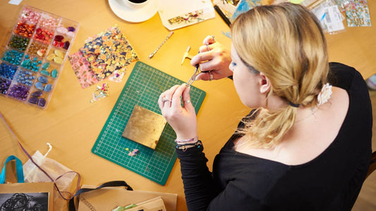 Overhead view of a jewelry maker working at a cluttered workspace with tools and materials, symbolizing the complexity of managing wholesale jewelry operations.