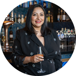 Sonal Pandya, jewelry designer at Aura Eternity, smiling while holding a glass of champagne in a black dress.