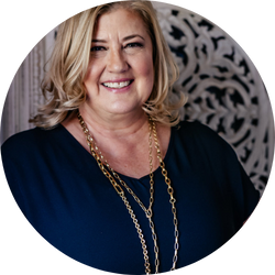 Loni Paul, jewelry designer with layered necklaces, smiling confidently in a black dress.