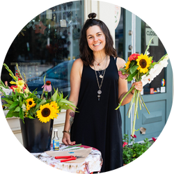 Brandy McNair, jewelry designer at Bella Vita, holding a bouquet of sunflowers, smiling outdoors.