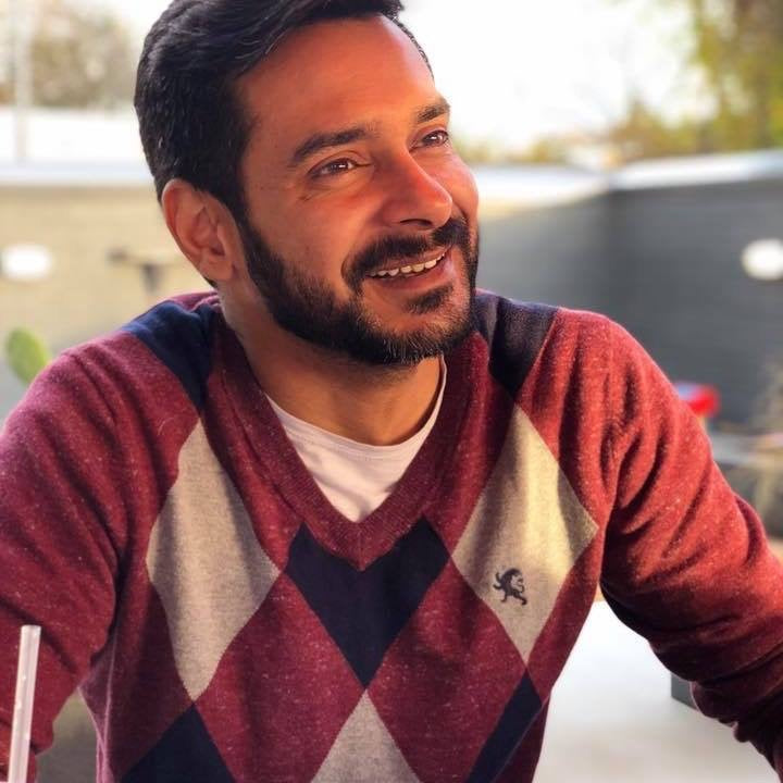 Portrait of Sohail A Dewani, founder of Jewelers League, wearing a white shirt and beaded bracelets, smiling warmly.