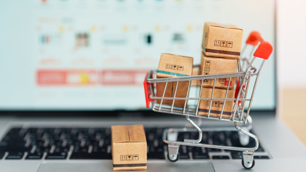 Mini shopping cart filled with boxes on a laptop, symbolizing the challenge of cart abandonment in e-commerce.