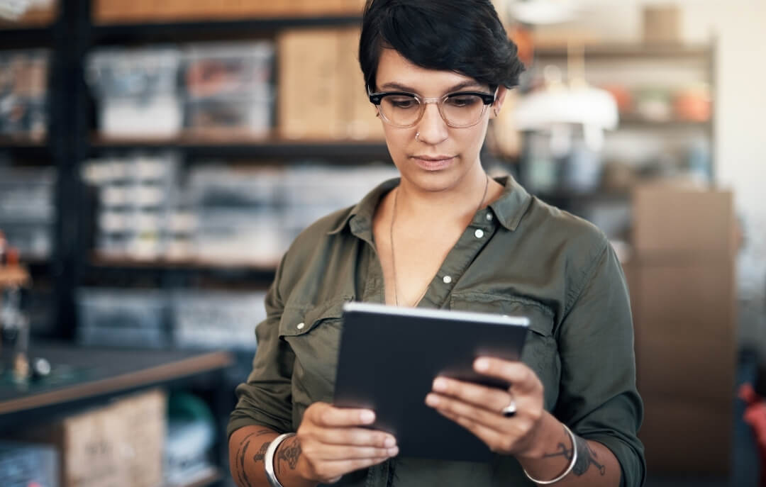 Female business owner using a tablet in a warehouse setting, representing inventory management and e-commerce operations.