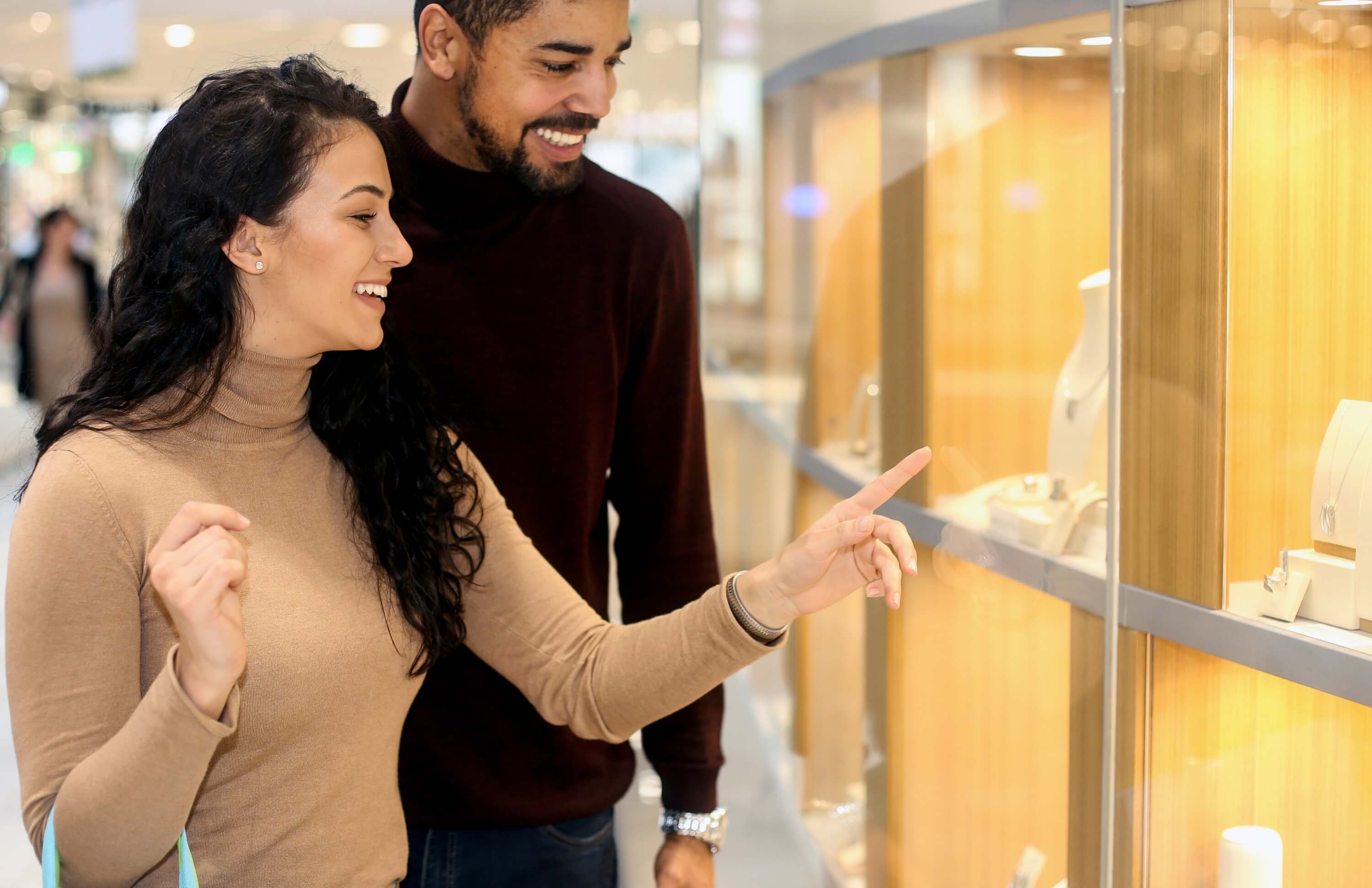 Couple shopping for jewelry, smiling and pointing at a display in a local store.